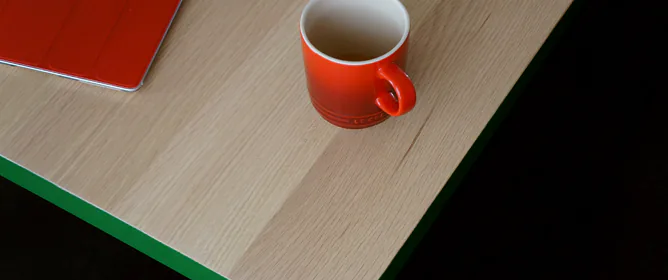 Een rode mok staat op een houten tafelblad; ernaast ligt een tabletcomputer met een rode beschermhoes.
